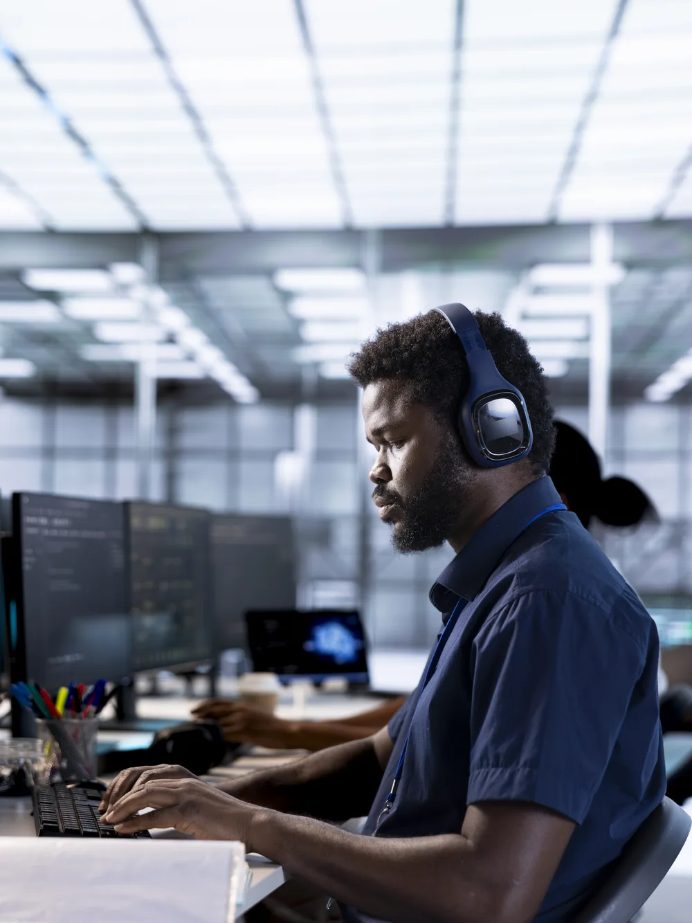 Engineer with headset working across multiple monitors in a modern tech office