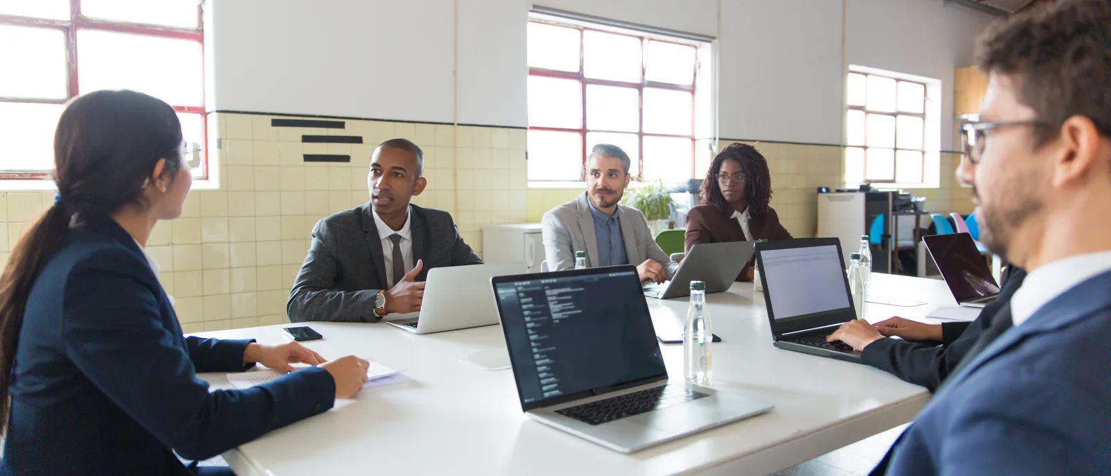 Team working through a plan together around a meeting table with laptops