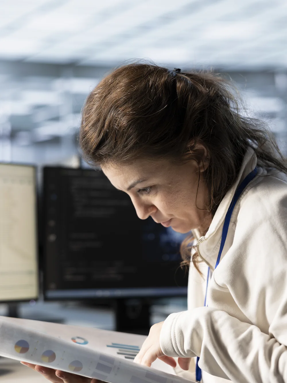 Woman reviewing printed records beside computer monitors