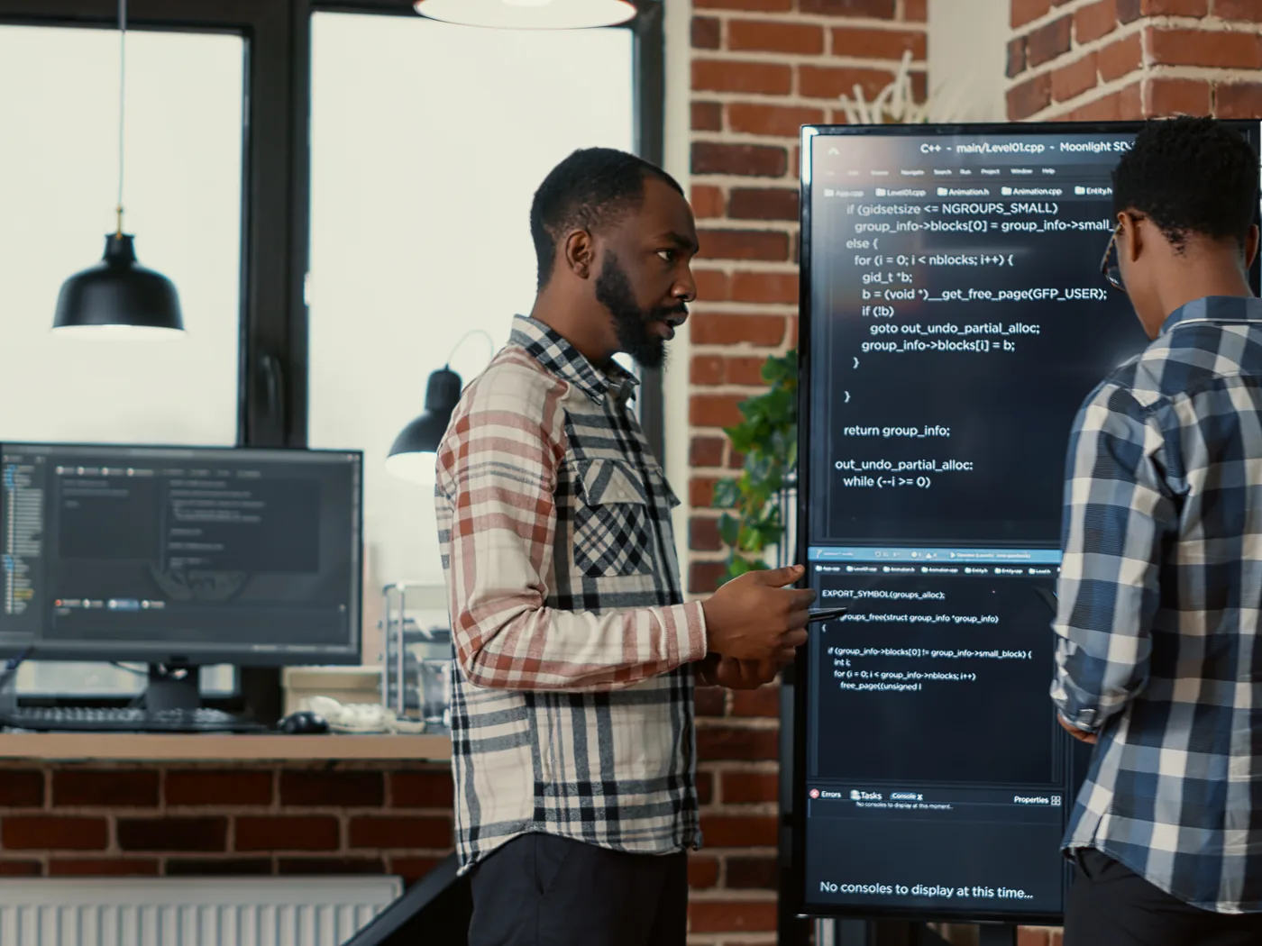 Two engineers comparing code on a large screen
