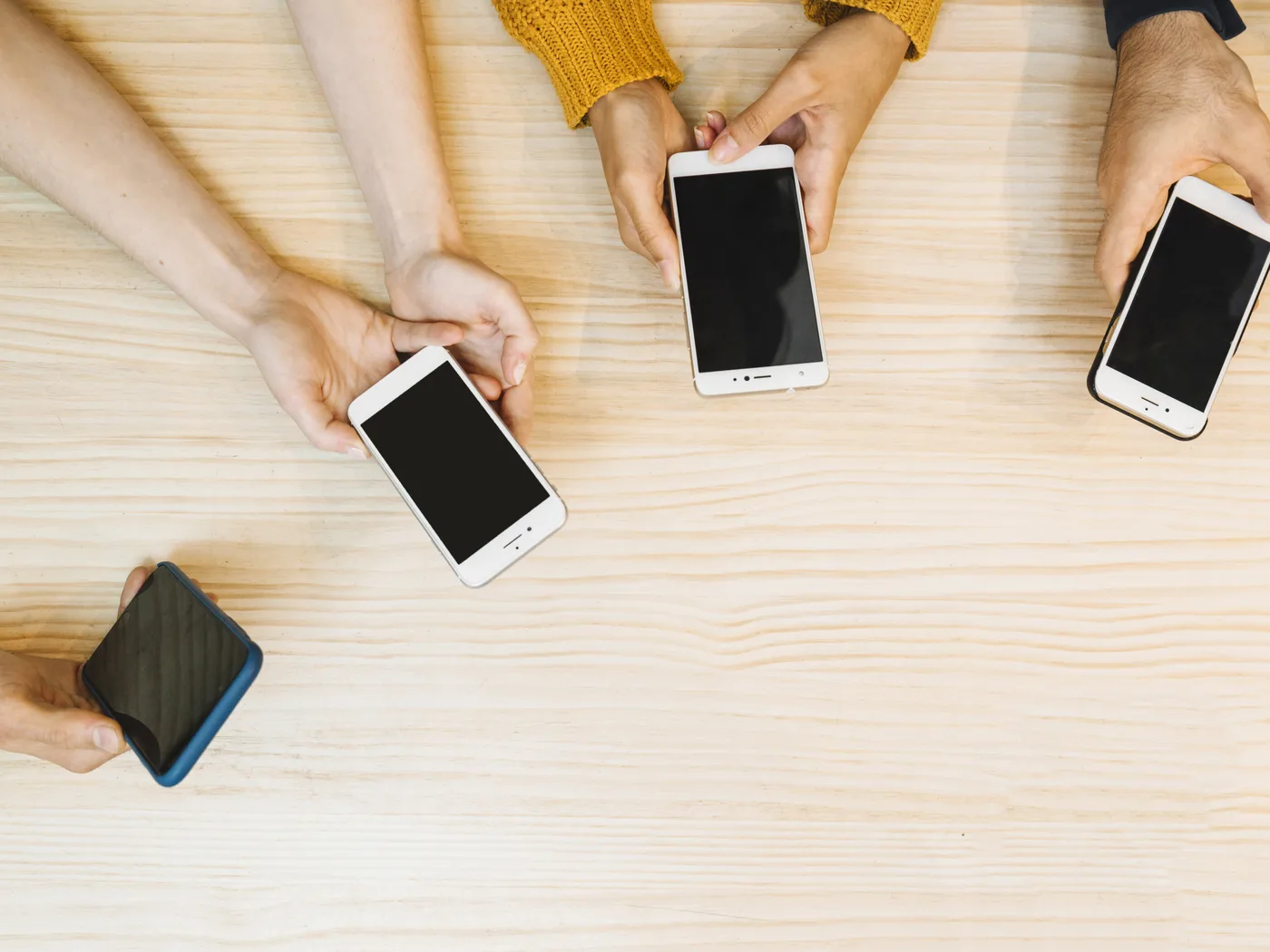Several hands using phones around a table